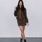 Woman wearing a brown jacket and skirt set with black boots on a plain background