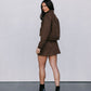 Woman wearing a brown outfit with black boots against a plain background
