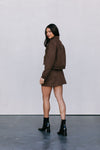 Woman wearing a brown outfit with black boots against a plain background