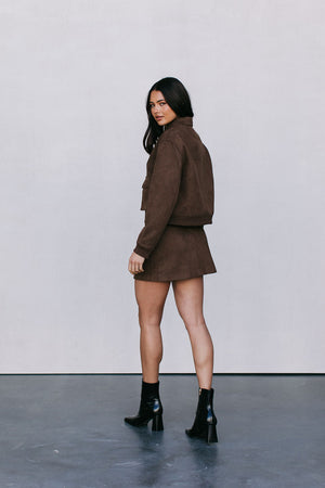Woman wearing a brown outfit with black boots against a plain background