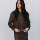 Woman wearing a brown jacket and skirt set against a plain background