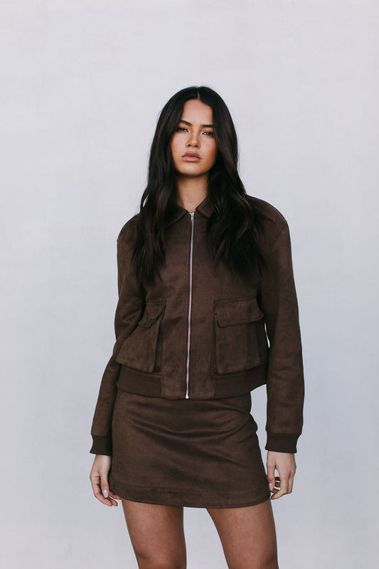 Woman wearing a brown jacket and skirt set against a plain background