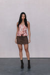 Woman wearing a floral top and brown skirt against a plain background