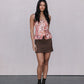 Woman wearing a floral top and brown skirt with black boots on a plain background