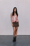 Woman wearing a floral top and brown skirt with black boots on a plain background