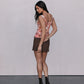 Woman wearing a floral top and brown skirt against a plain background
