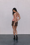 Woman wearing a floral top and brown skirt against a plain background