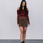 Woman wearing a burgundy off-shoulder top and brown suede skirt against a white background