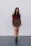 Woman wearing a burgundy off-shoulder top and brown suede skirt against a white background