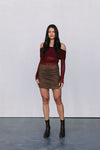 Woman wearing a burgundy off-shoulder top and brown skirt against a plain background