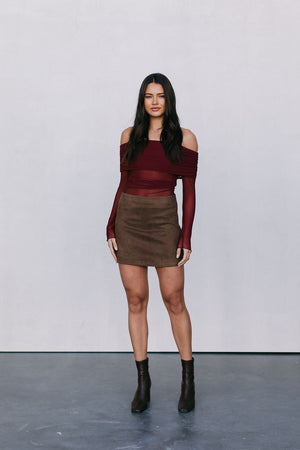 Woman wearing a burgundy off-shoulder top and brown skirt against a plain background