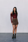 Woman wearing a burgundy off-shoulder top and brown skirt against a white background