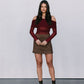 Woman wearing a burgundy off-shoulder top and brown skirt with black boots against a plain background