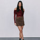 Woman wearing a burgundy off-shoulder top and brown suede skirt against a white background