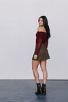 Woman wearing a burgundy off-shoulder top and brown skirt with black boots against a white background