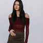 Woman wearing a burgundy off-shoulder top and brown suede skirt against a plain background