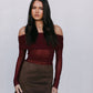 Woman wearing a burgundy off-shoulder top and brown skirt against a white background