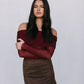 Woman wearing a burgundy off-shoulder top and brown skirt against a plain background