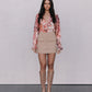 Woman wearing a floral blouse, beige skirt, and tan boots against a plain background