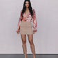 Woman wearing a floral blouse, beige skirt, and tan boots against a plain background