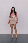 Woman wearing a floral blouse, beige skirt, and tan boots against a plain background