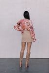 Person wearing a floral blouse, beige skirt, and tan knee-high boots against a plain background
