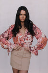 Woman wearing a floral blouse and beige skirt against a plain background