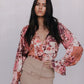 Woman wearing a floral blouse and beige skirt against a plain background