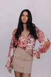 Woman wearing a floral blouse and beige skirt against a plain background