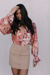 Woman wearing a floral blouse and beige skirt against a white background
