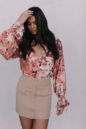 Woman wearing a floral blouse and beige skirt against a white background
