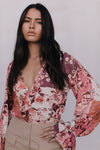 Woman wearing a floral blouse with long sleeves against a plain background