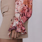 Close-up of a person wearing a floral blouse with ruffled sleeves and beige shorts.