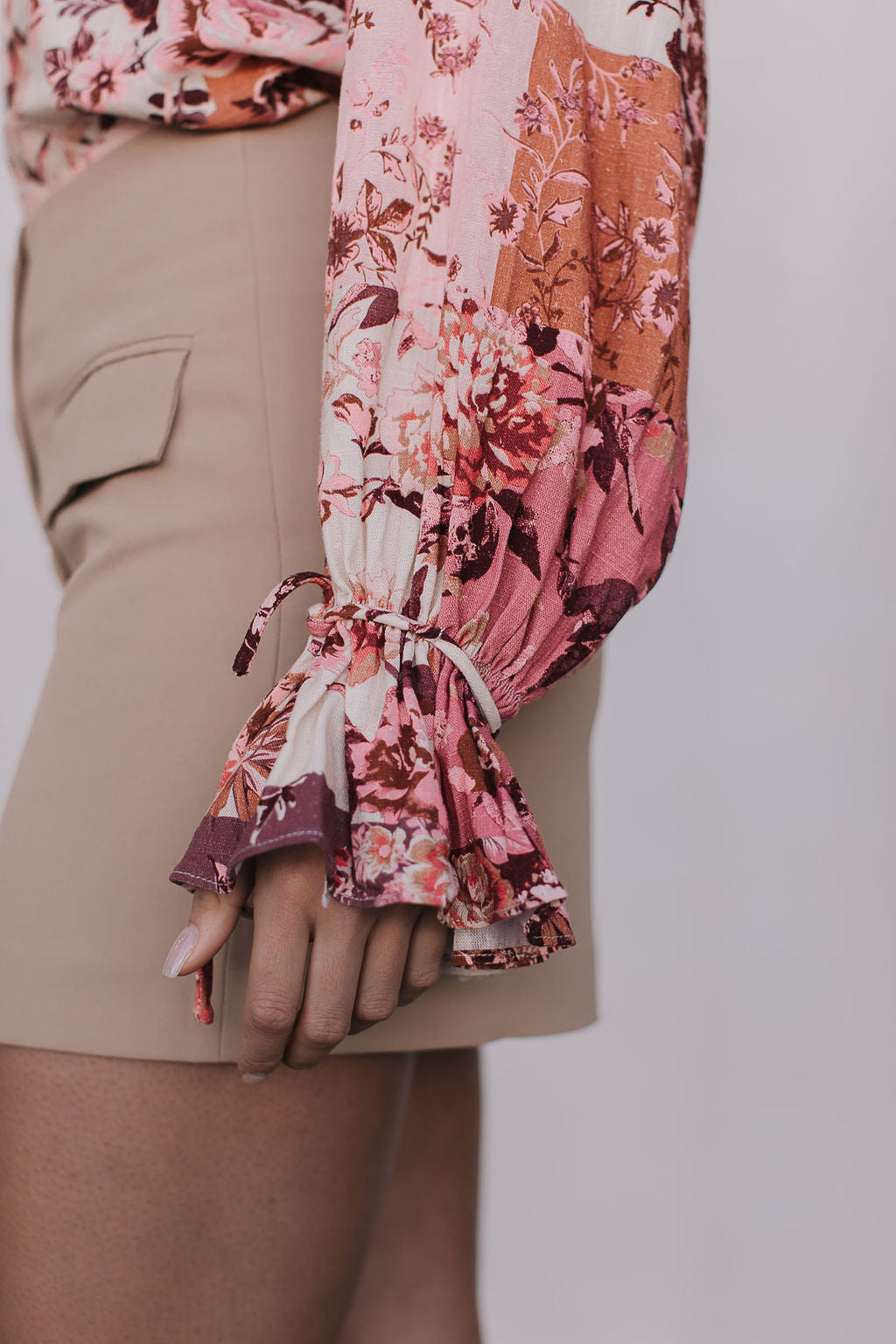 Close-up of a person wearing a floral blouse with ruffled sleeves and beige shorts.