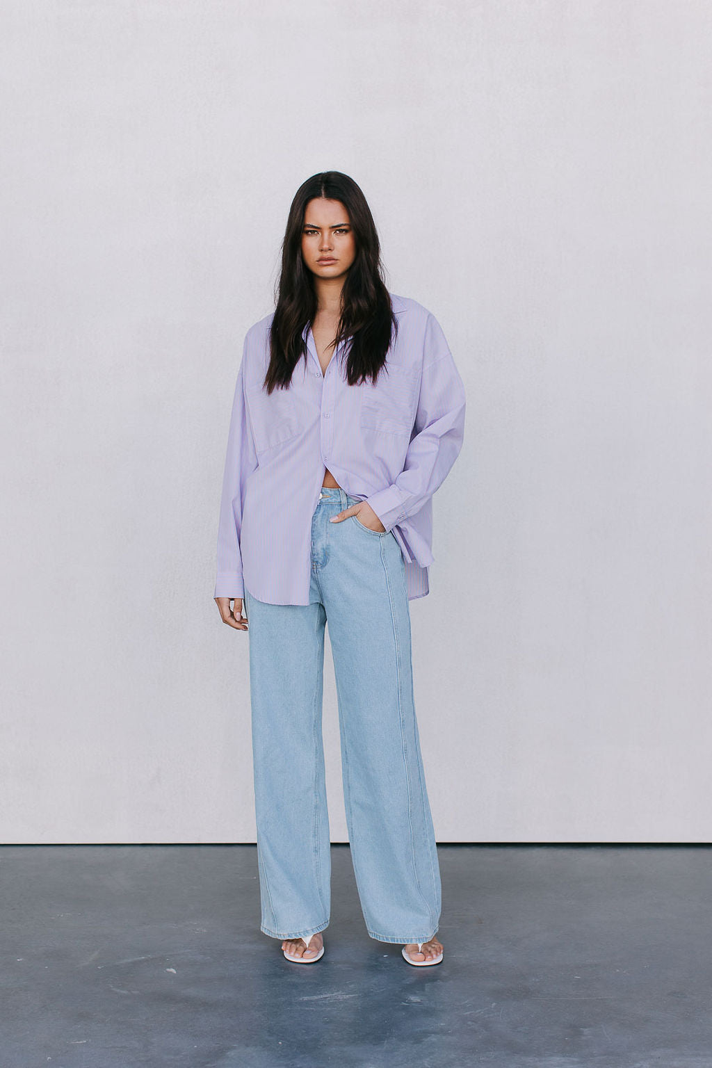 Woman wearing a light purple shirt and light blue jeans against a white background
