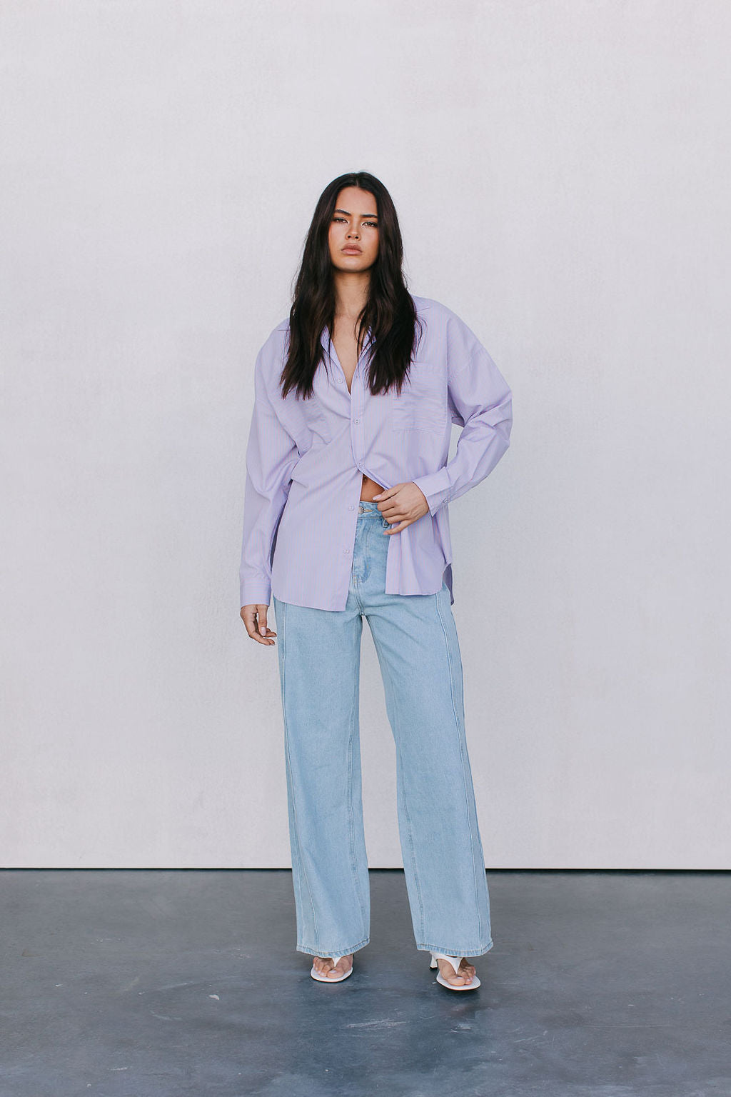 Woman wearing a light purple shirt and light blue jeans against a white background