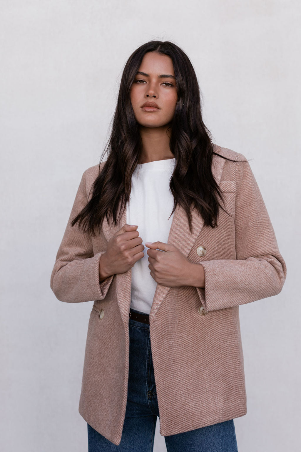 Woman wearing a beige coat over a white shirt with a plain background