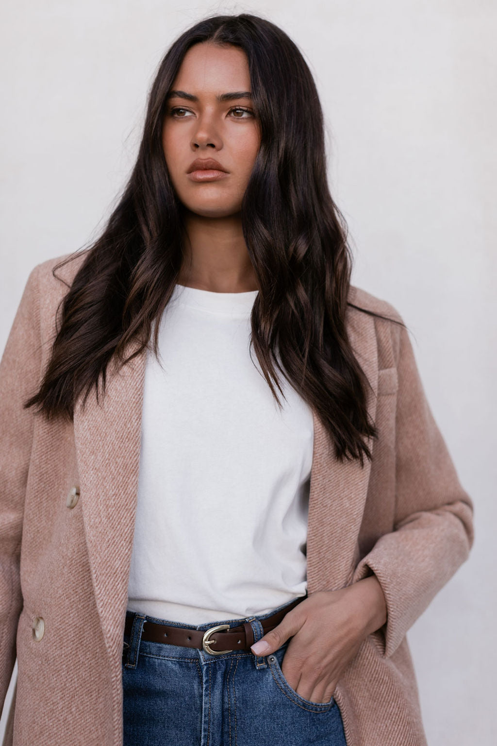 Woman wearing a beige coat over a white shirt with a plain background