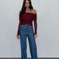 Woman wearing a burgundy off-shoulder top and blue jeans against a plain background