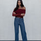 Woman wearing a burgundy off-shoulder top and blue jeans against a plain background