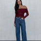 Woman wearing a burgundy off-shoulder top and blue jeans against a plain background