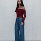 Woman wearing a burgundy off-shoulder top and blue jeans against a white background