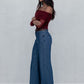 Woman wearing a burgundy top and blue jeans against a plain background