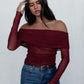 Woman wearing a burgundy off-shoulder top and blue jeans against a white background