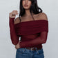 Woman wearing a burgundy off-shoulder top and blue jeans against a white background