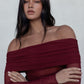 Woman wearing a burgundy off-shoulder top against a plain background