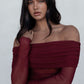 Woman wearing a burgundy off-shoulder top and blue jeans against a white background