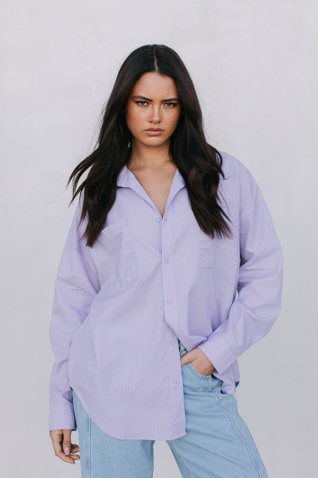 Woman wearing a light purple shirt and light blue jeans against a plain background