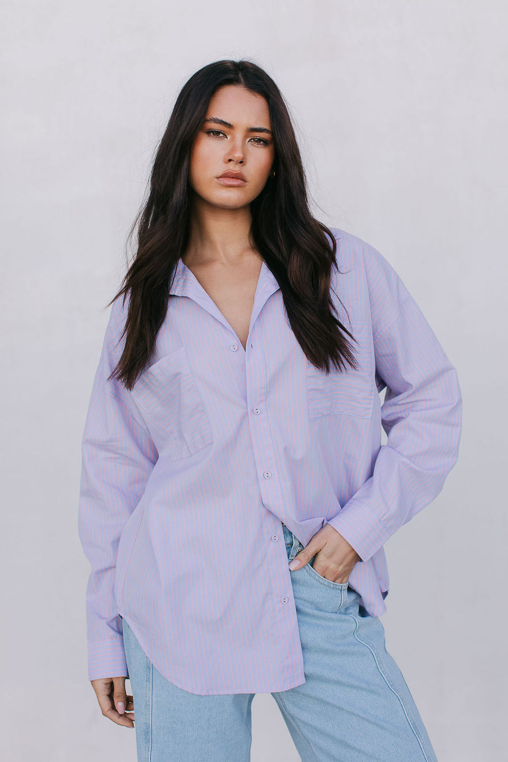 Woman wearing a light purple shirt and light blue jeans against a plain background