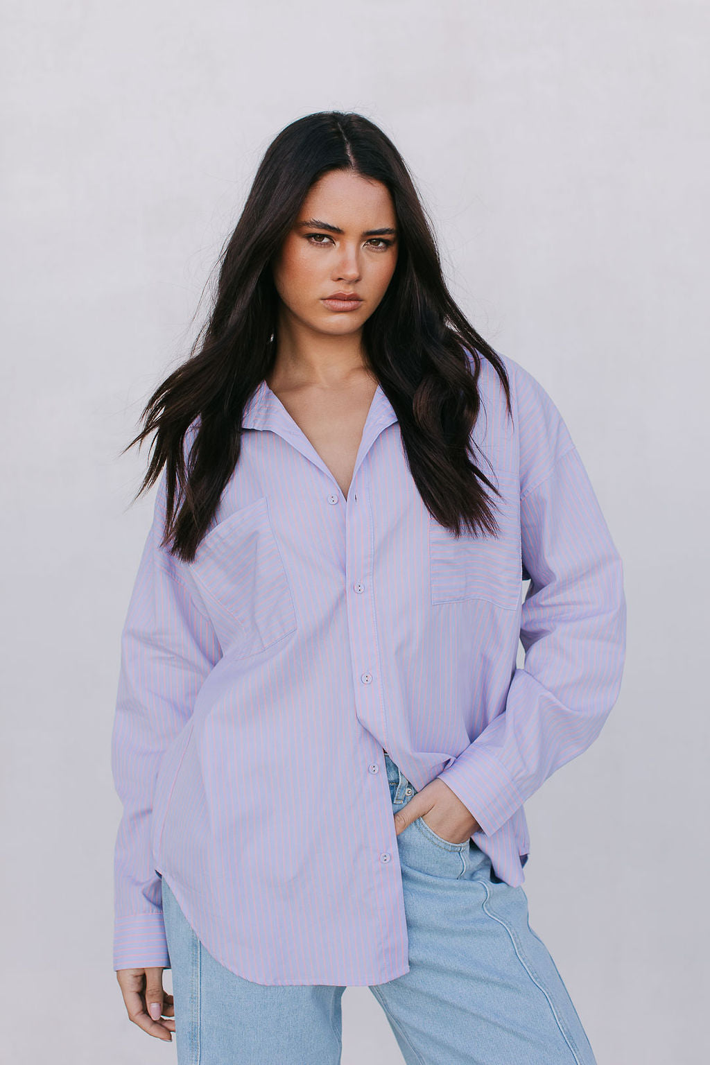 Woman wearing a light purple shirt and light blue jeans against a plain background